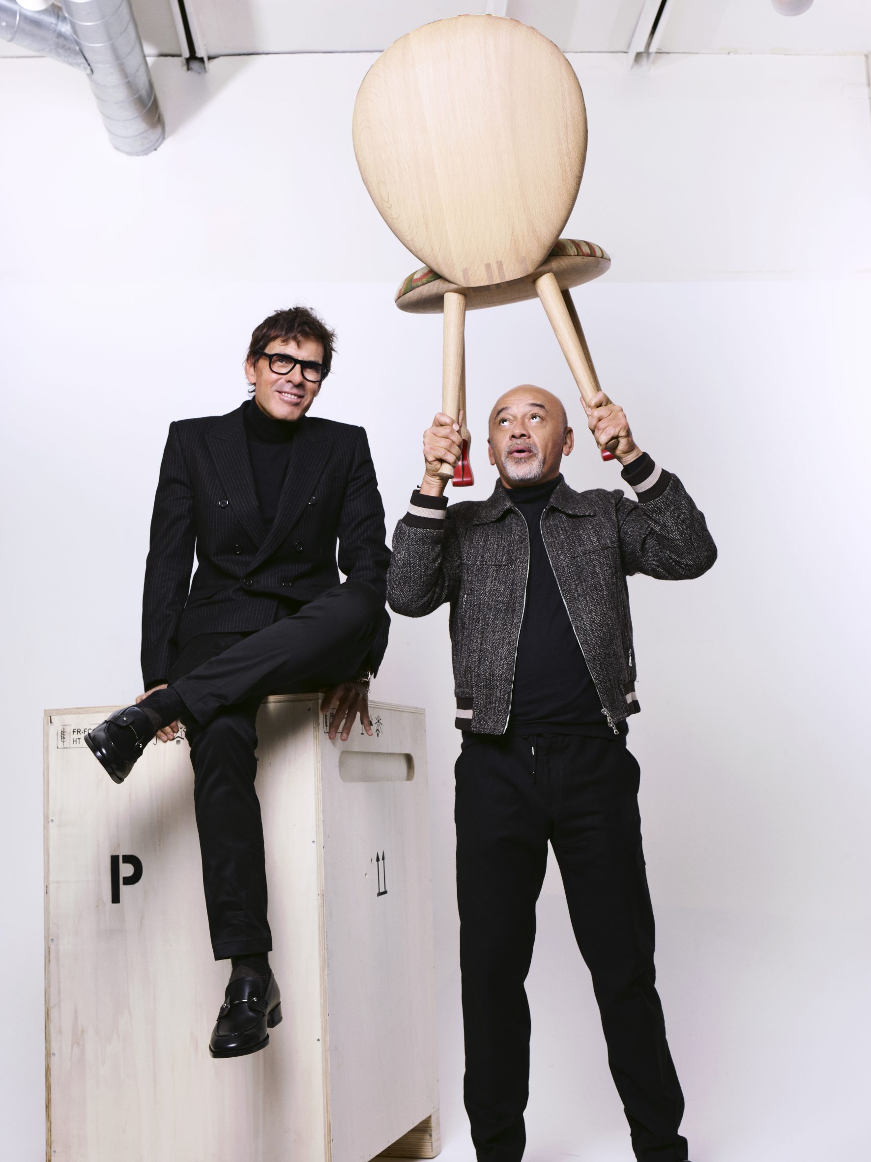 Portrait shot of Pierre Yovanovitch and Christian Louboutin lifting a chair