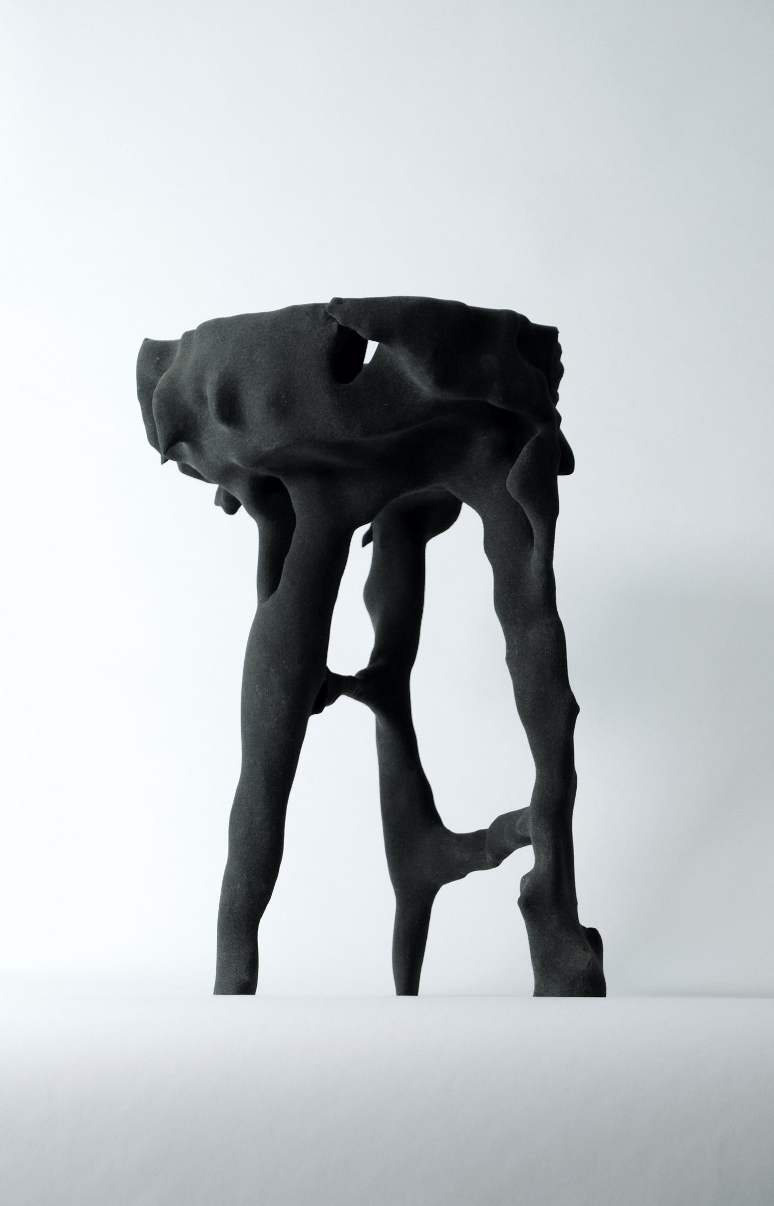 Photo of a gnarled, complex-shaped three-legged stool in a matt black material