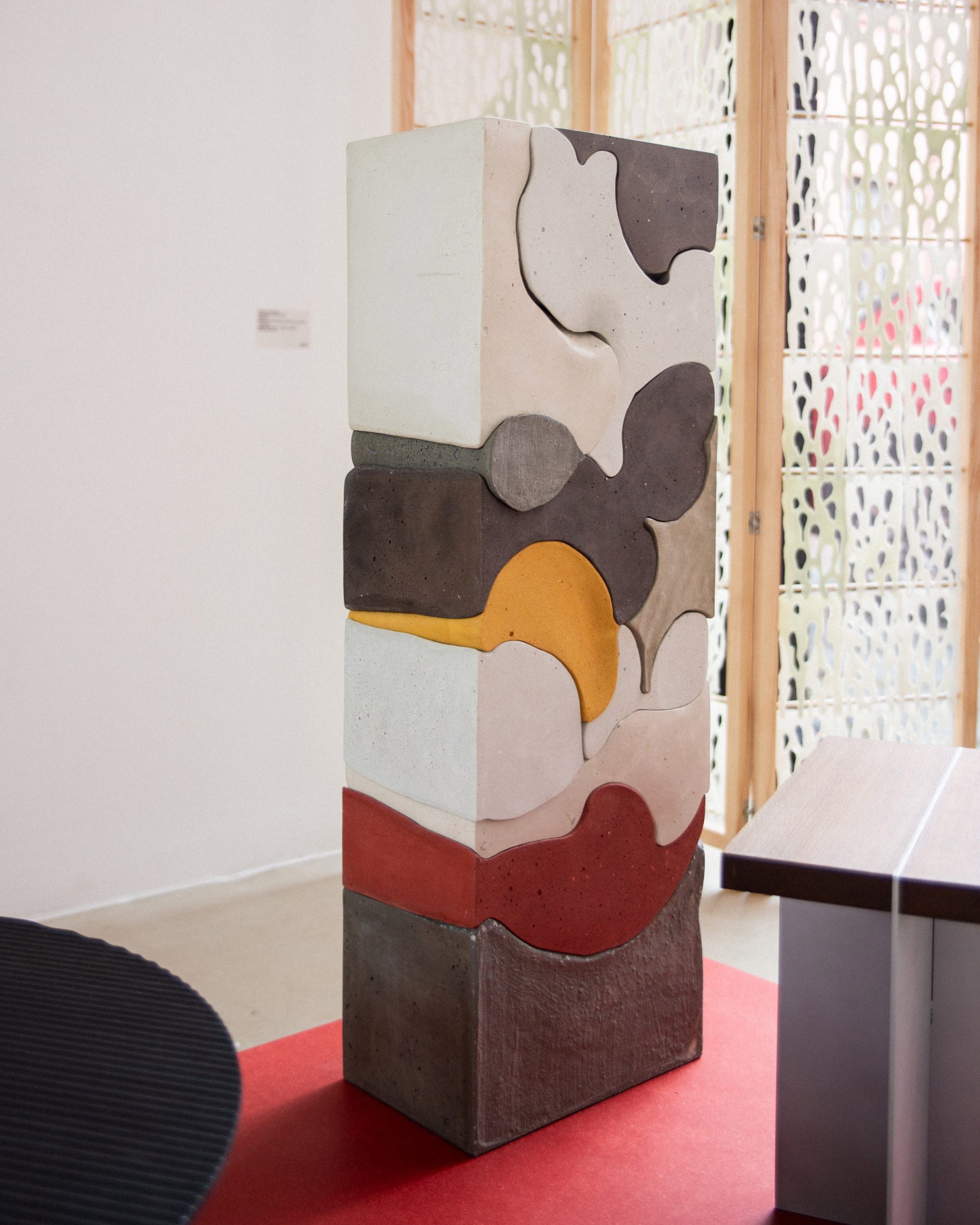 A photograph of a rectangular sculpture made of cement in tones of grey, red, yellow and white, on display in the Under One Roof exhibition.